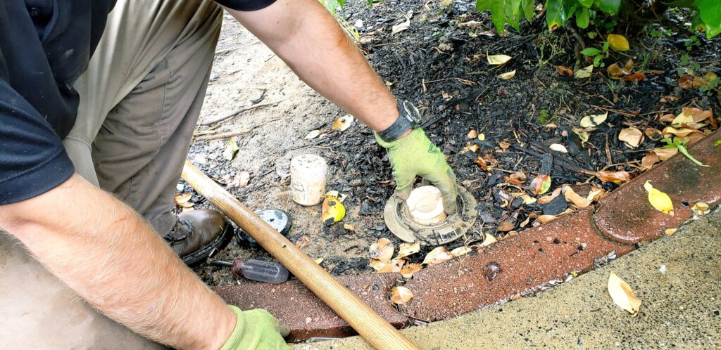 Exterminator at a home inserting termite traps into soil around house.