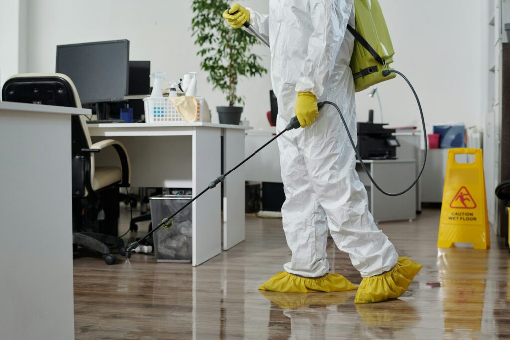 Young male worker of cleaning service in protective workwear spraying floor